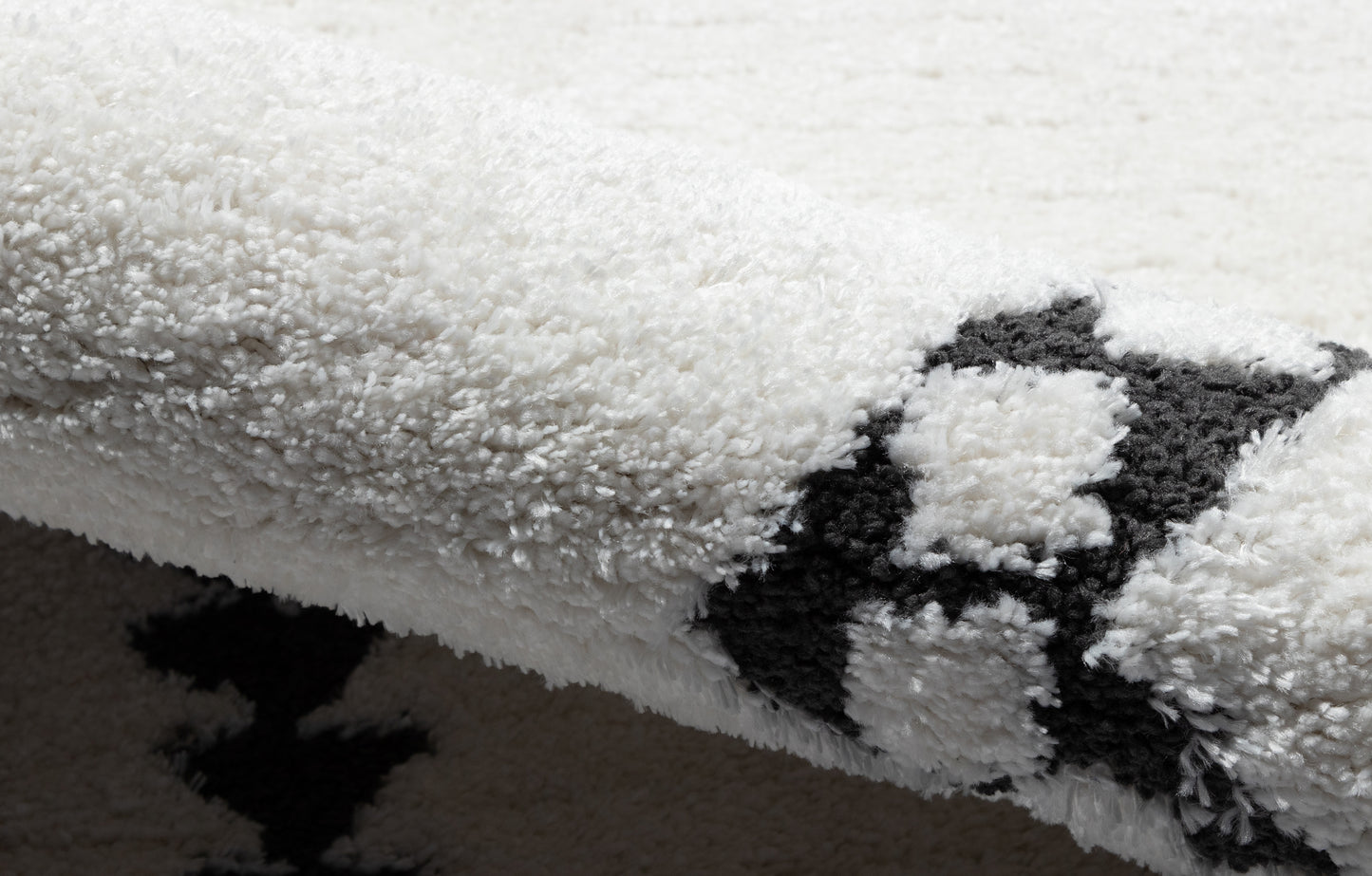 Close-up of white plush shag rug with a black geometric pattern; 5' x 7' rug, soft high-pile texture for modern home decor.
