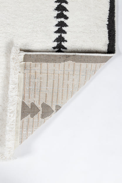 Ivory rug with black border pattern; folded corner reveals beige woven underside with geometric triangles; fringed trim.
