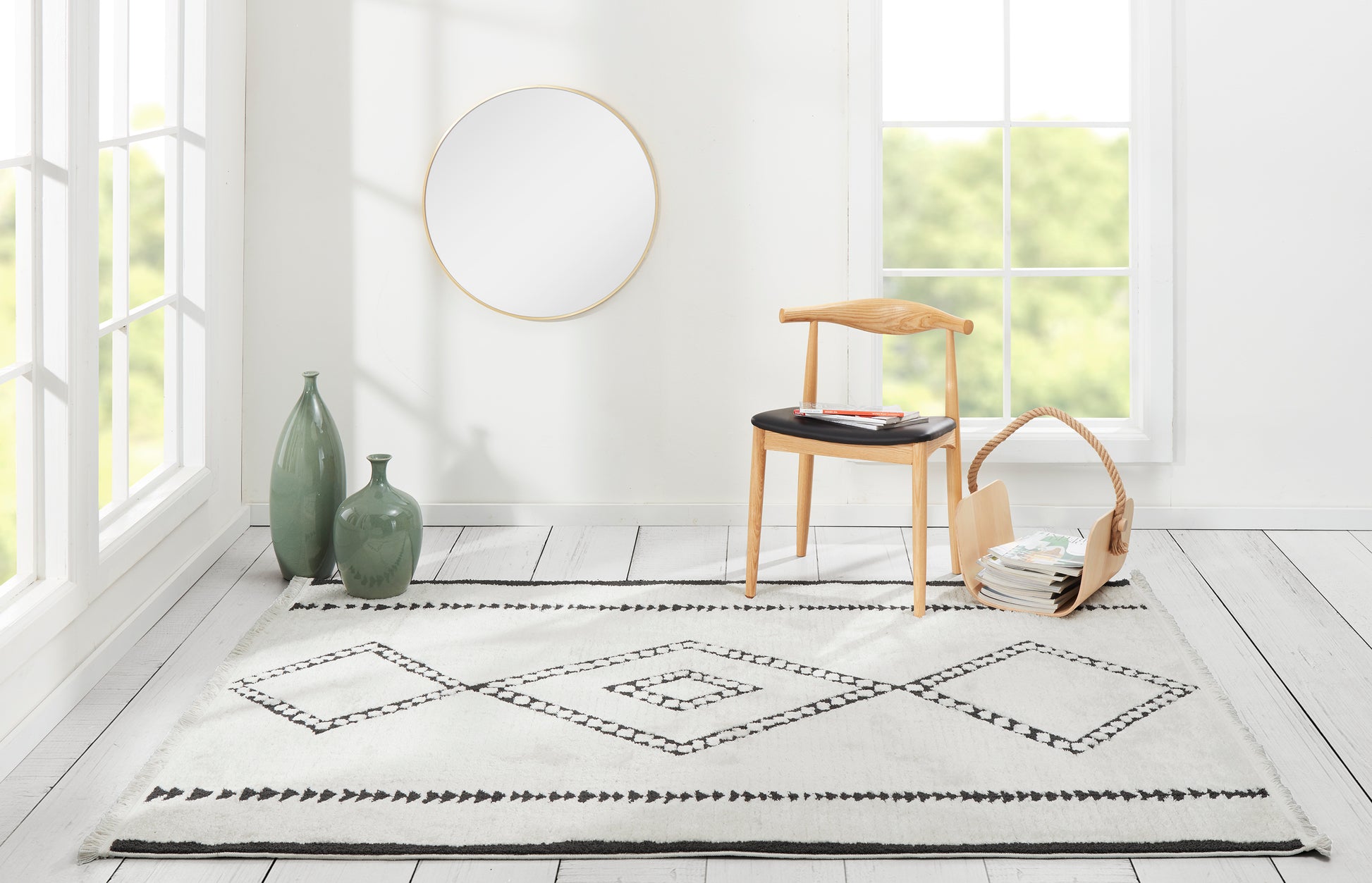 Minimalist living room rug with black diamond border, light wood chair, gold-framed mirror, green vases, wicker basket.