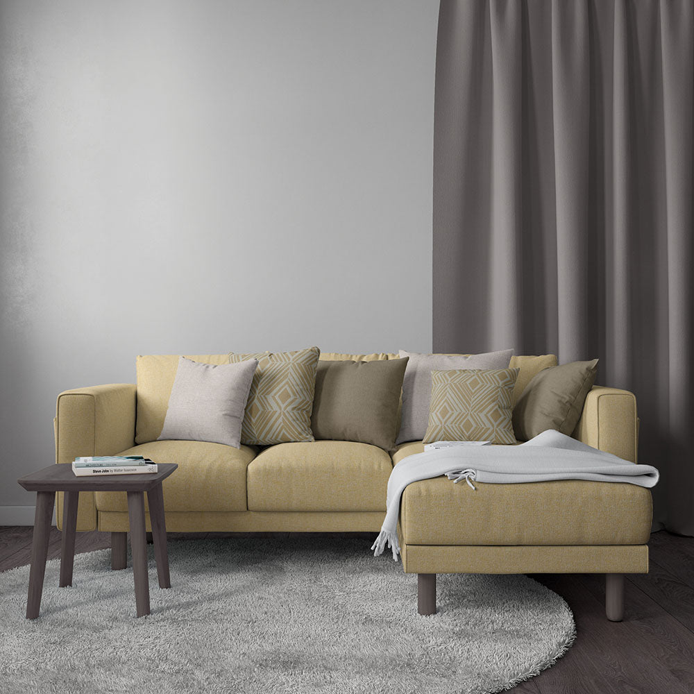 Mustard fabric sectional with chaise, dark wood round side table, gray cushions and throw in a gray living room.