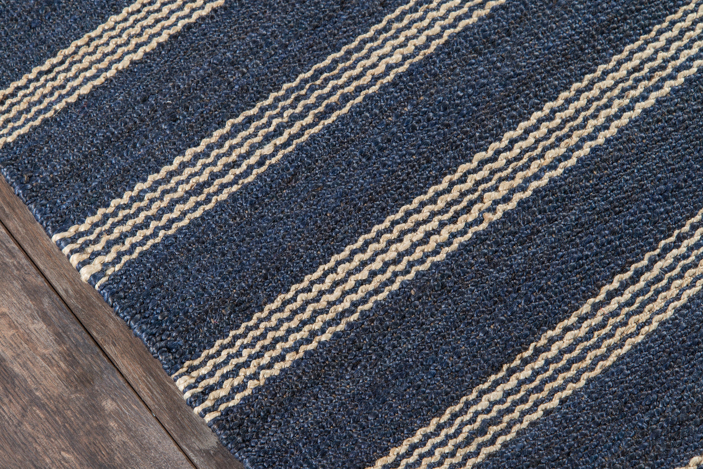Navy blue rectangular rug with beige braided stripes on dark wood floor.