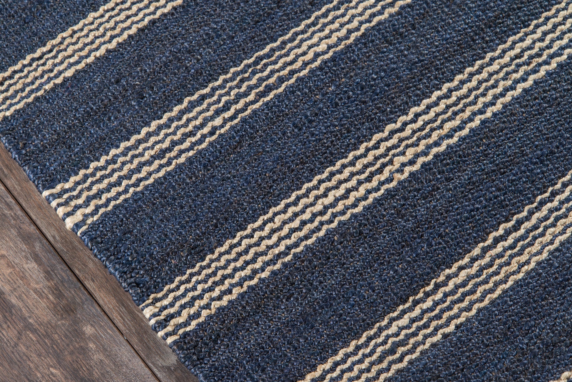 Navy blue rectangular rug with beige braided stripes on dark wood floor.
