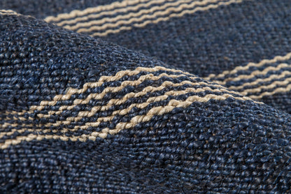 Close-up of dark indigo denim rug with beige woven stripes; rugged, textured blue textile.