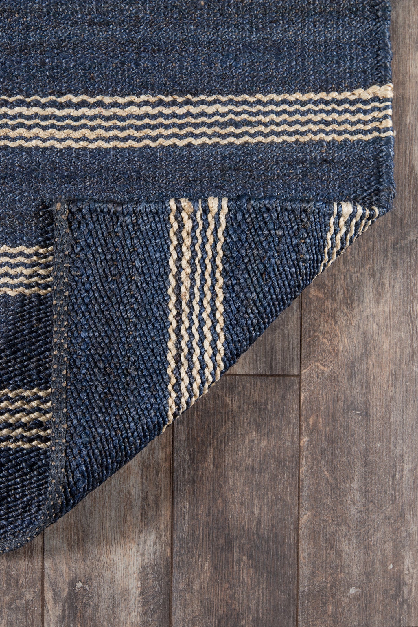 Navy blue flatweave rug with natural beige stripes; folded corner on wood floor.