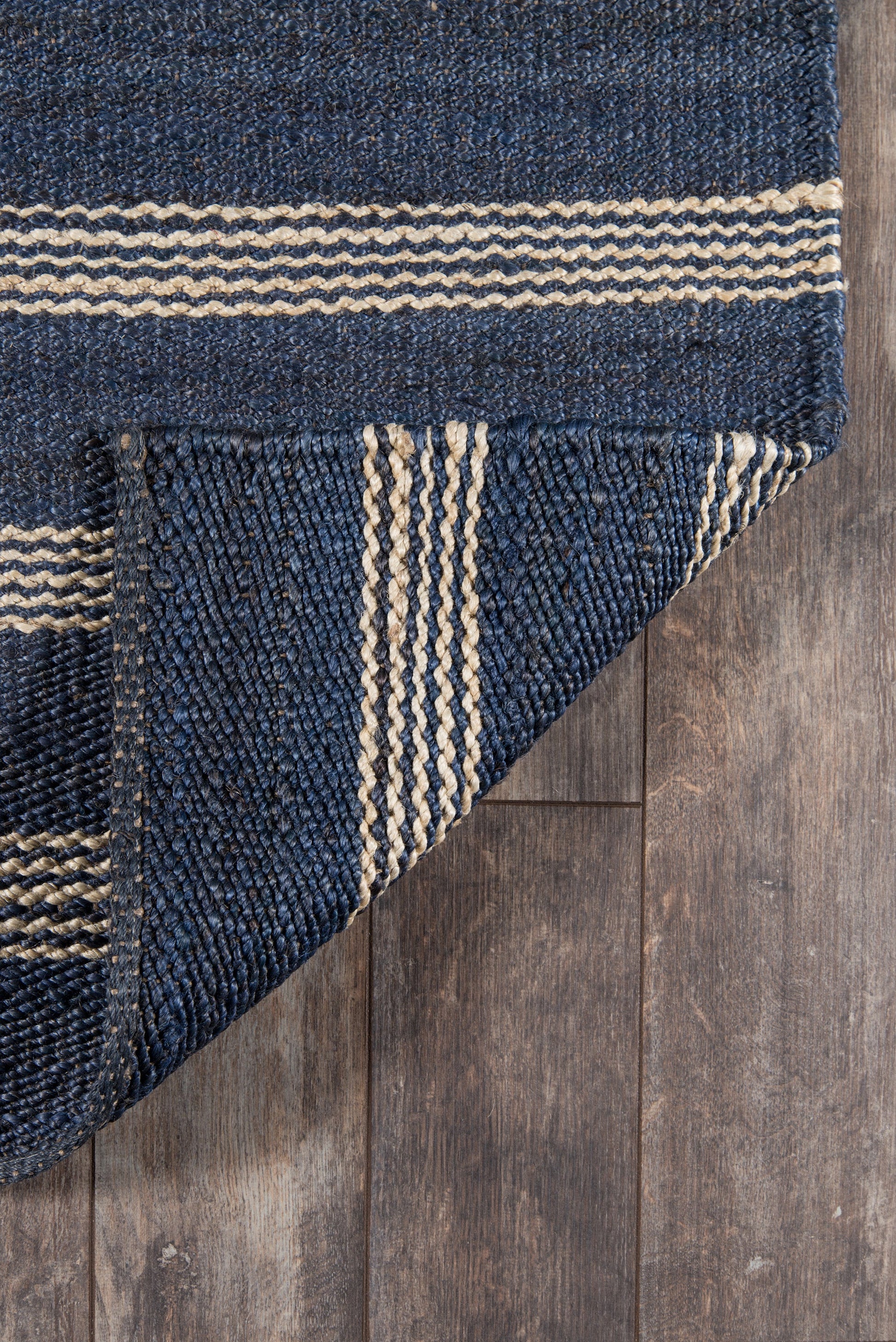 Navy blue flatweave rug with natural beige stripes; folded corner on wood floor.
