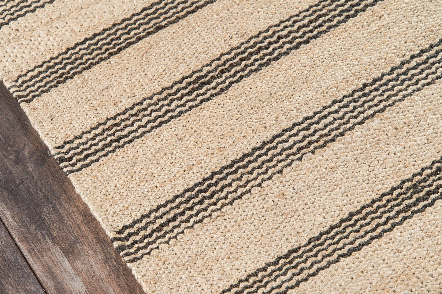Beige natural jute rug with dark striped bands on a dark wood floor.