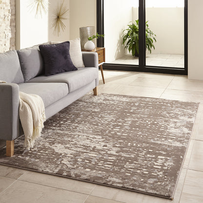 Gray fabric sofa with wooden legs on a taupe abstract rug; beige throw, dark pillow, sunlit living room with glass doors.