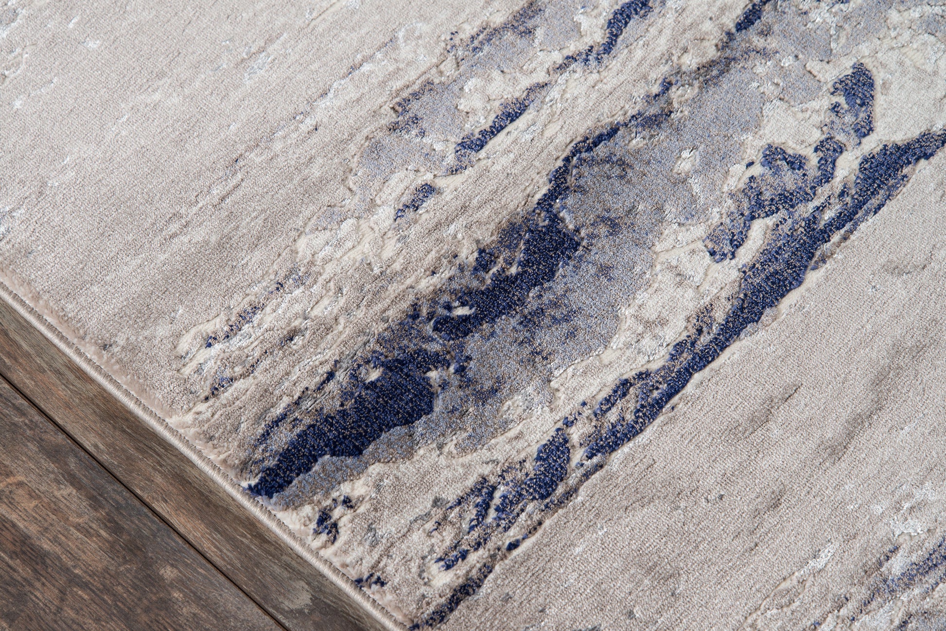 Beige & navy abstract rug on wooden floor; contemporary woven textile with blue wave pattern.