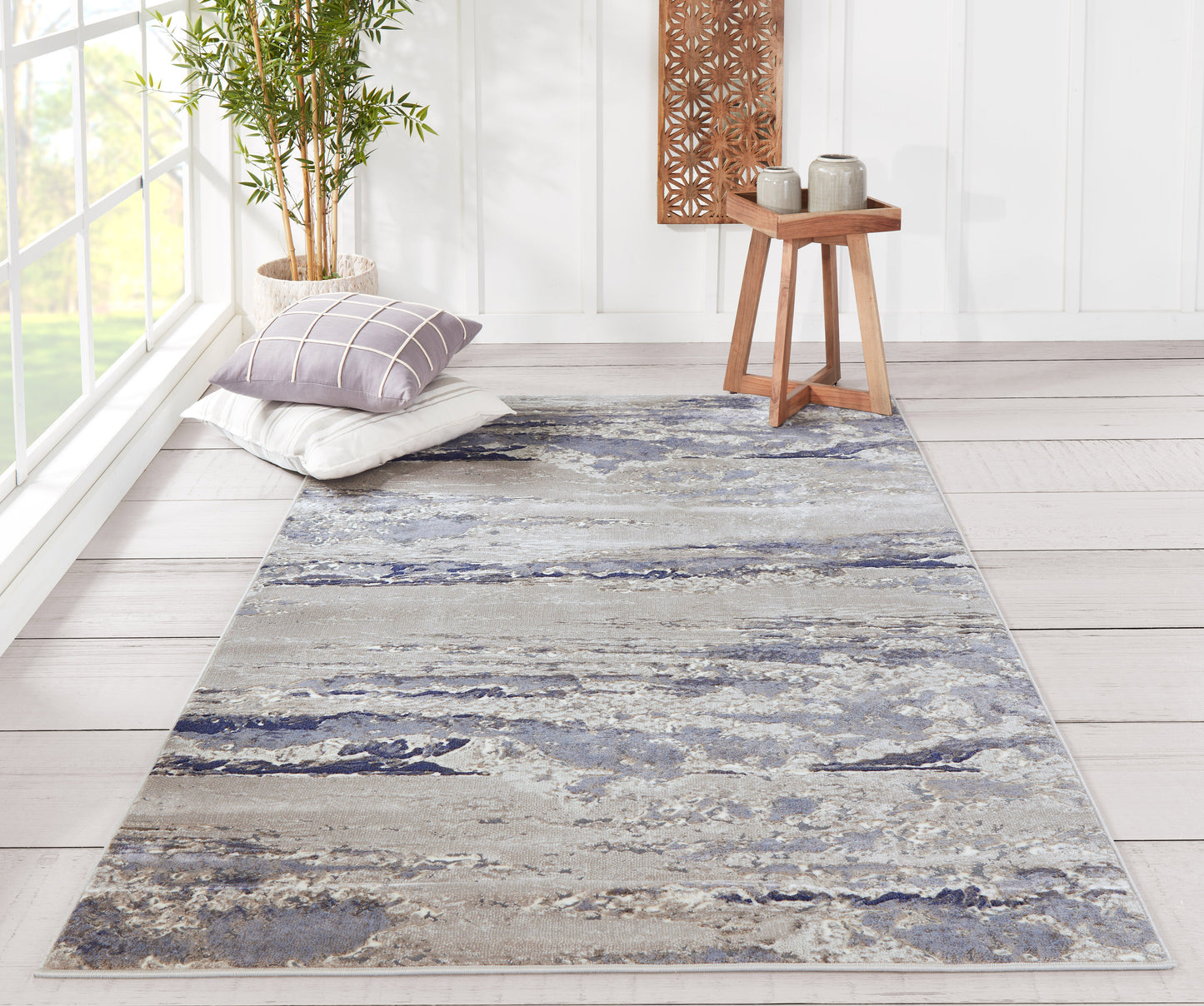 Blue-gray marbled rectangular rug (2' x 3') in a bright living room with pillows, a plant, and a wooden side table.