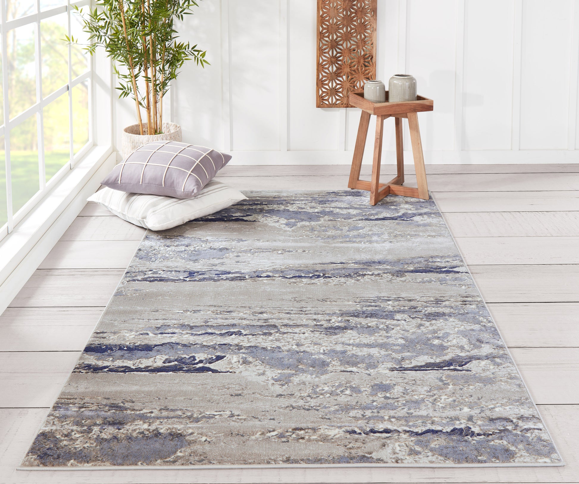 Blue-gray marbled rectangular rug (2' x 3') in a bright living room with pillows, a plant, and a wooden side table.