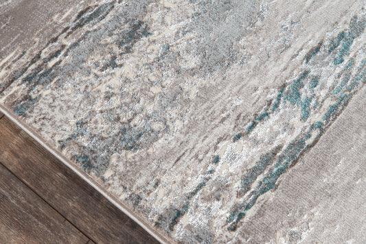 Close-up of a textured abstract area rug in gray, teal and beige on dark wood flooring.