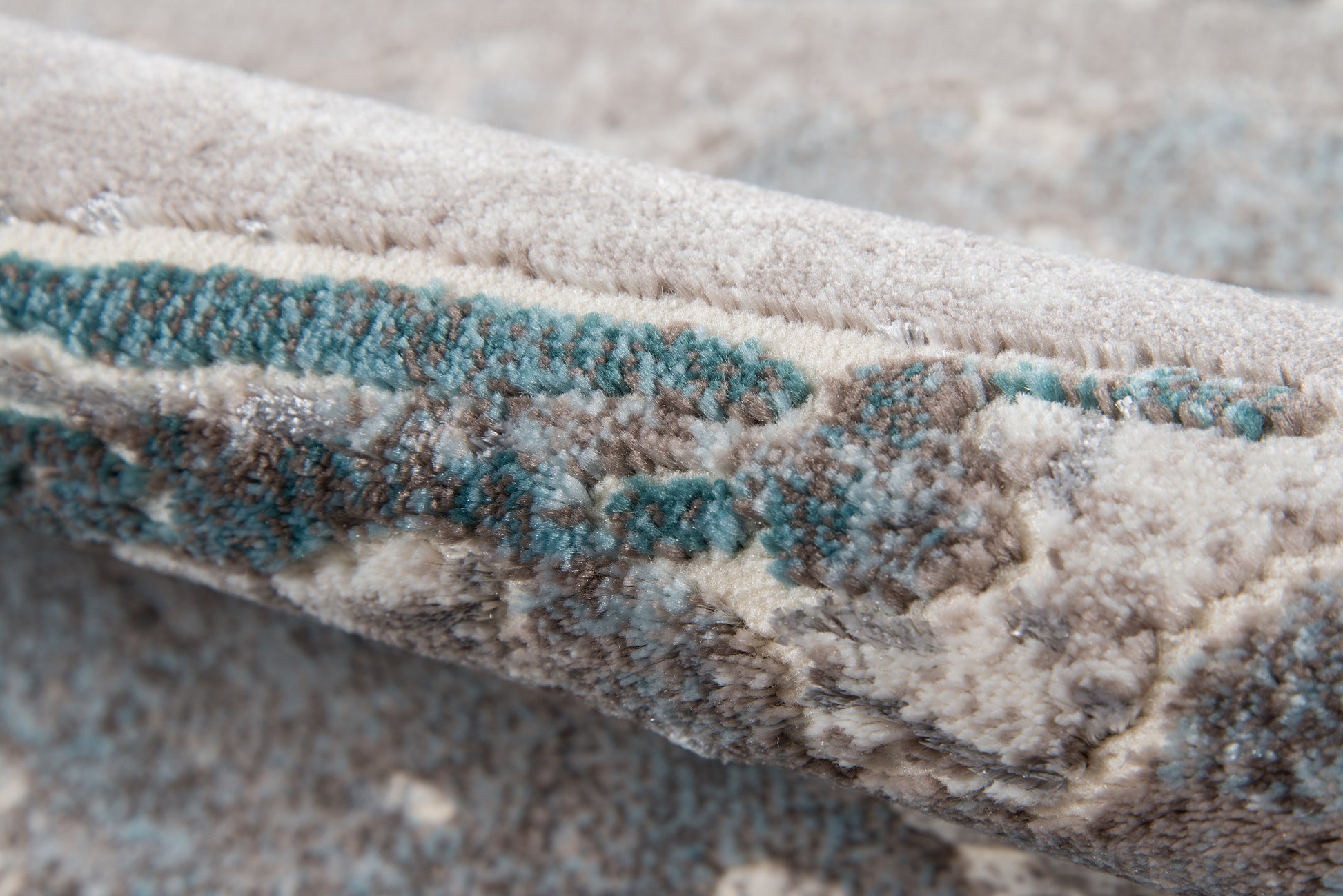 Beige and cream textured rug with teal abstract accents, thick plush pile and folded edge.