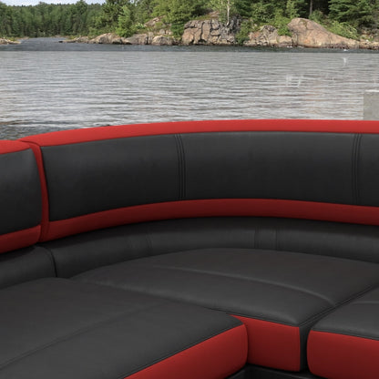 Curved seating upholstered in red solid fabric with cushioned backrests, shown beside a lake with a rocky shoreline and trees in the background.