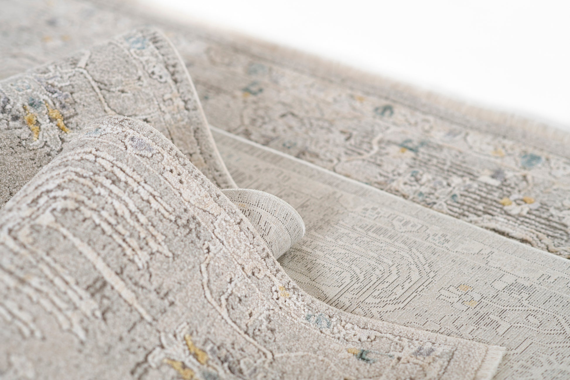Gray Moroccan-style rug with cream motifs and subtle yellow and blue accents; rolled edge shows soft textured pile.
