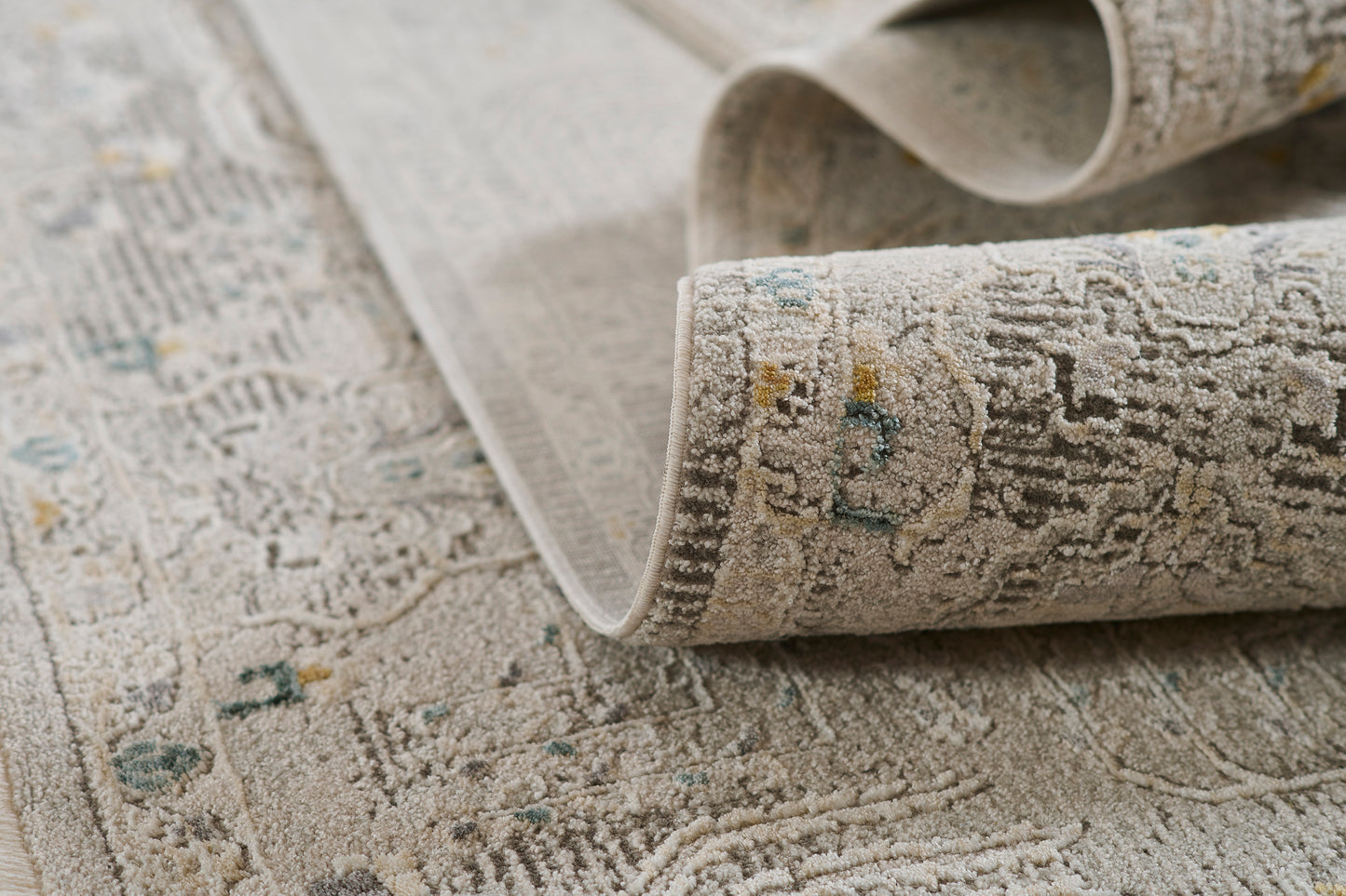Gray oriental rug with faded floral motif, plush pile, rolled edge, beige-gray tones with teal and yellow accents.