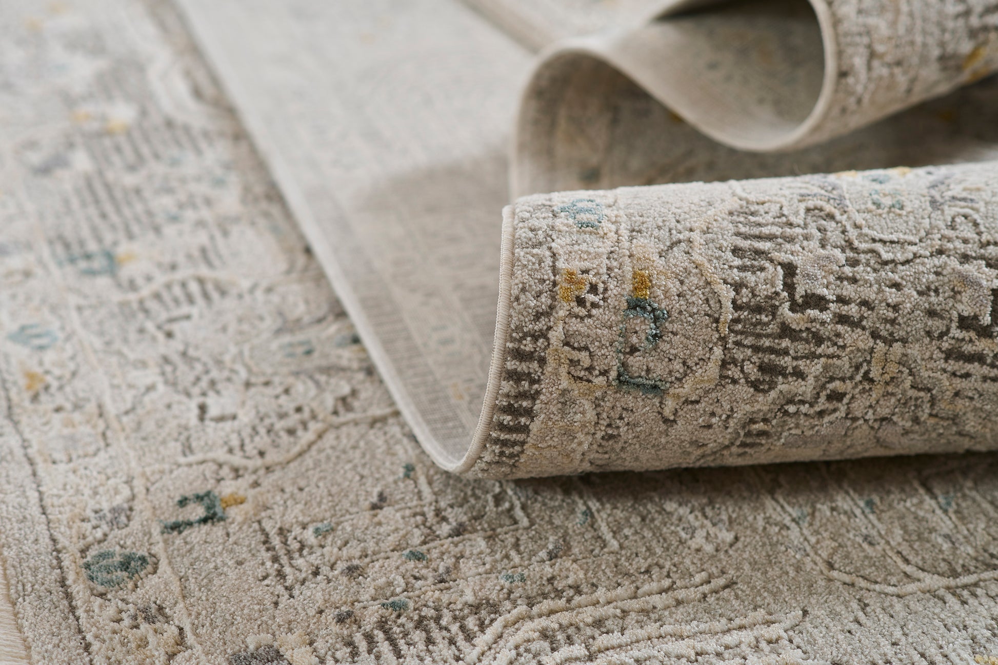 Beige-gray oriental area rug with a distressed floral pattern, teal and yellow accents; rolled corner.