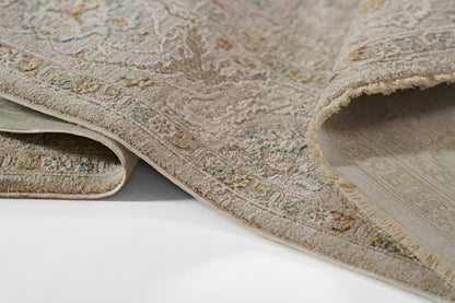 Beige ornate rug with subtle multicolor floral motifs, plush pile, folded edge showing backing.