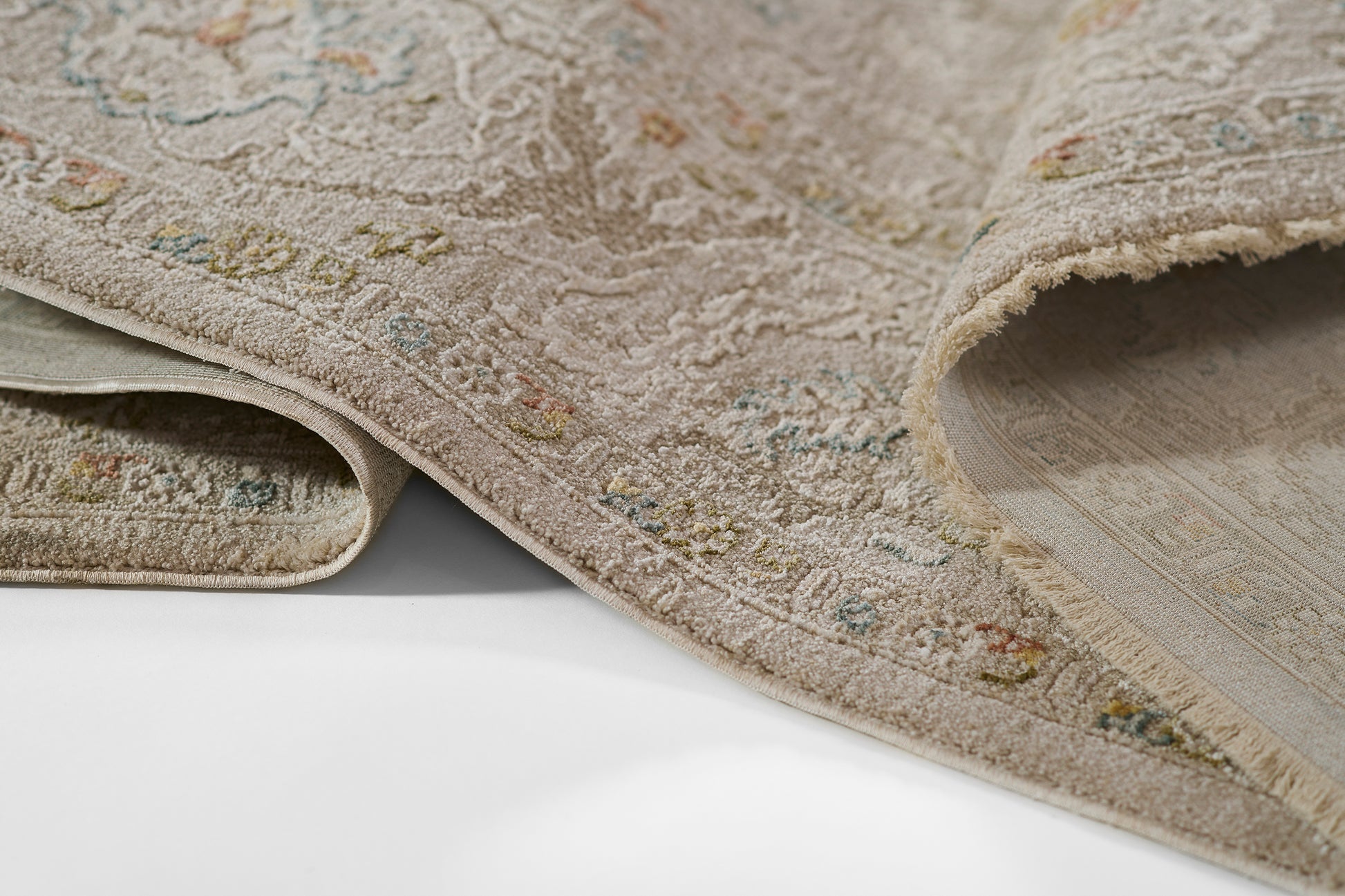 Beige oriental rug with pastel floral motifs, plush textured pile, folded edge revealing underside; ideal for living rooms.