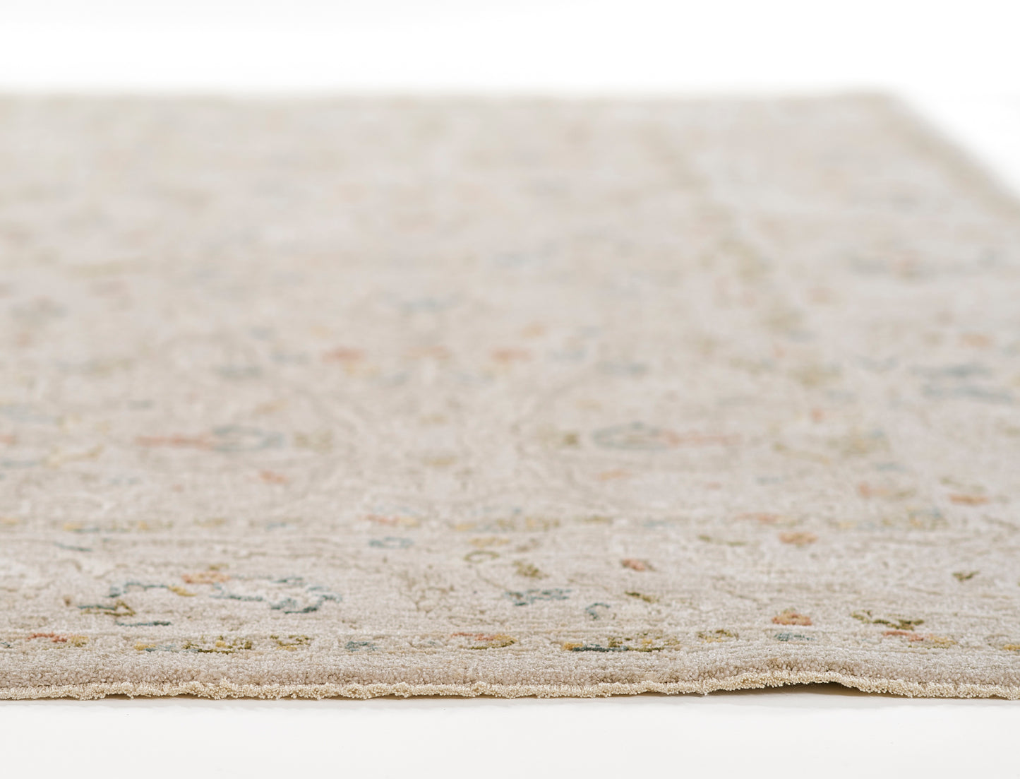Beige rectangular rug with subtle pastel floral motifs in blue, green and pink; fringed edges, soft tufted texture.