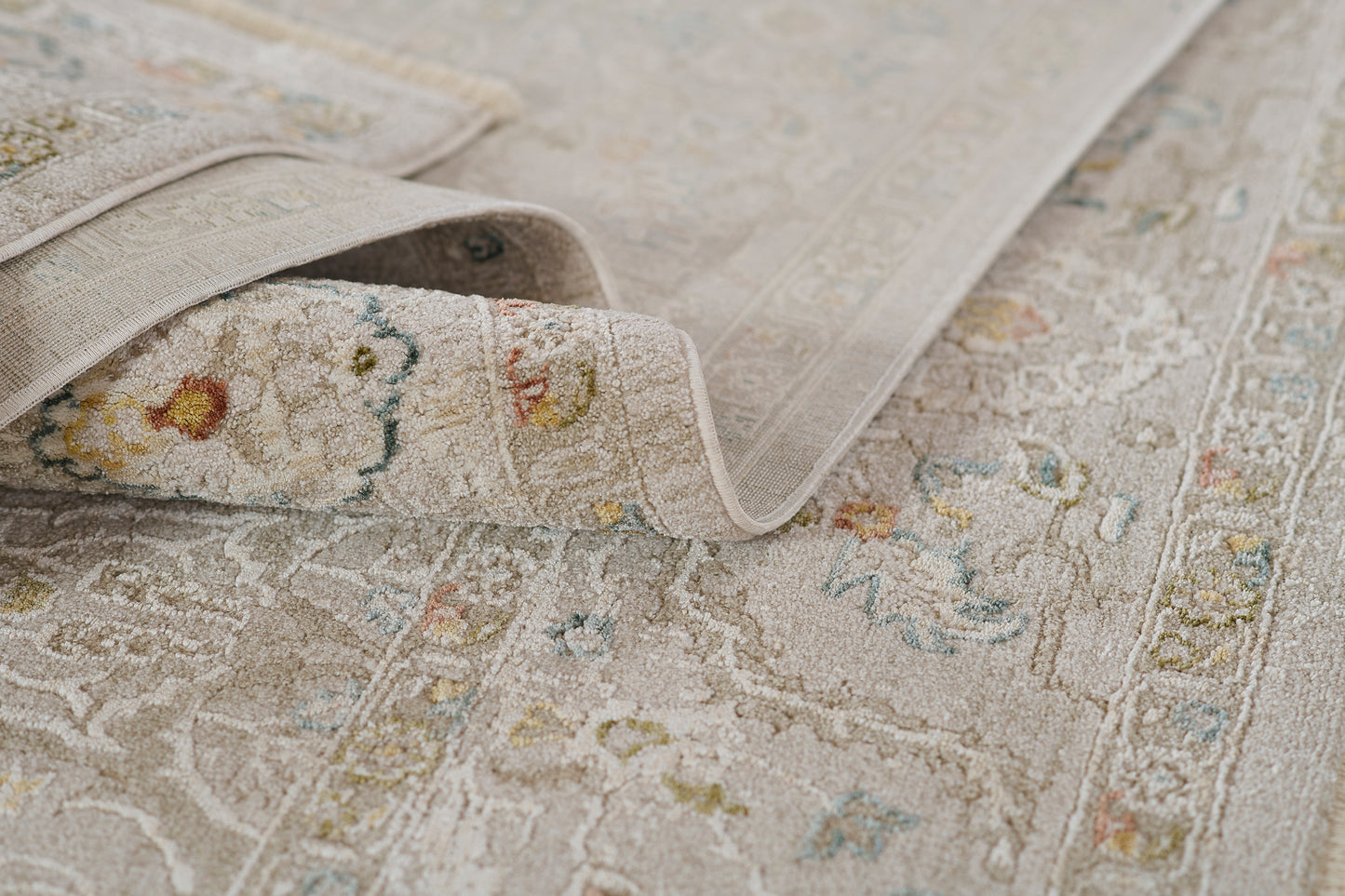 Beige oriental-inspired rug with subtle floral motifs, distressed ivory border, soft textured pile and rolled edge.