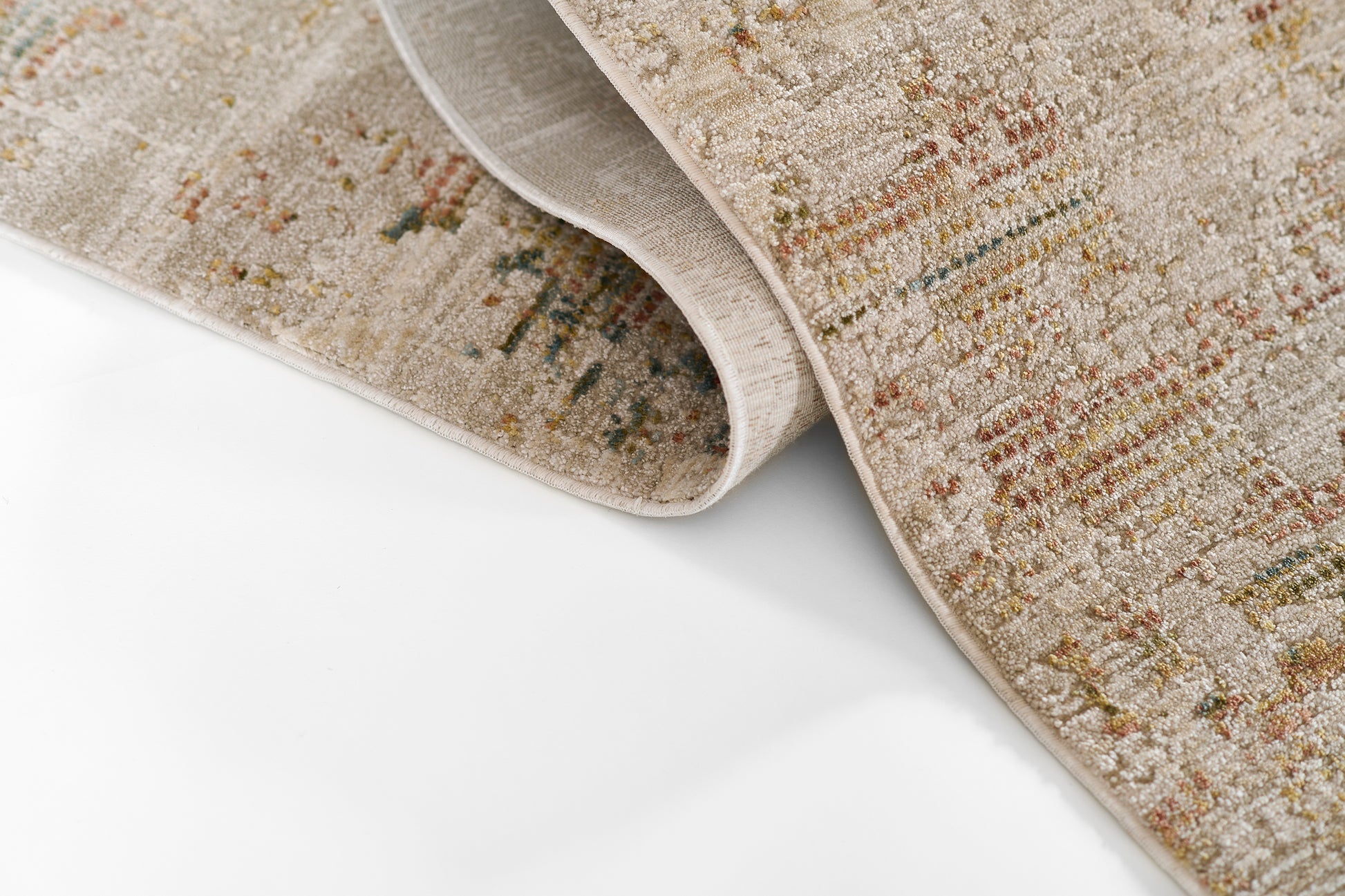 Beige textured area rug with muted multicolor streaks; rolled at the corner on a white surface.