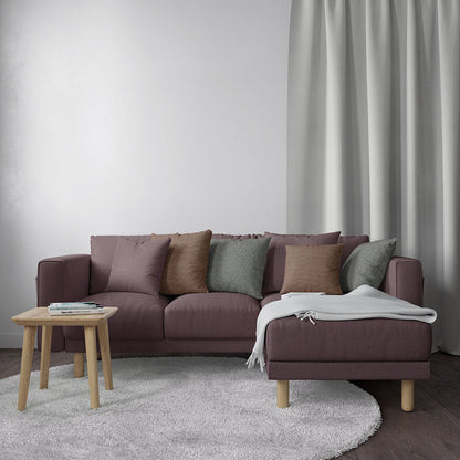 Dusty mauve L-shaped fabric sofa with chaise, earth-toned cushions, light wood legs, gray throw, beside a round coffee table.