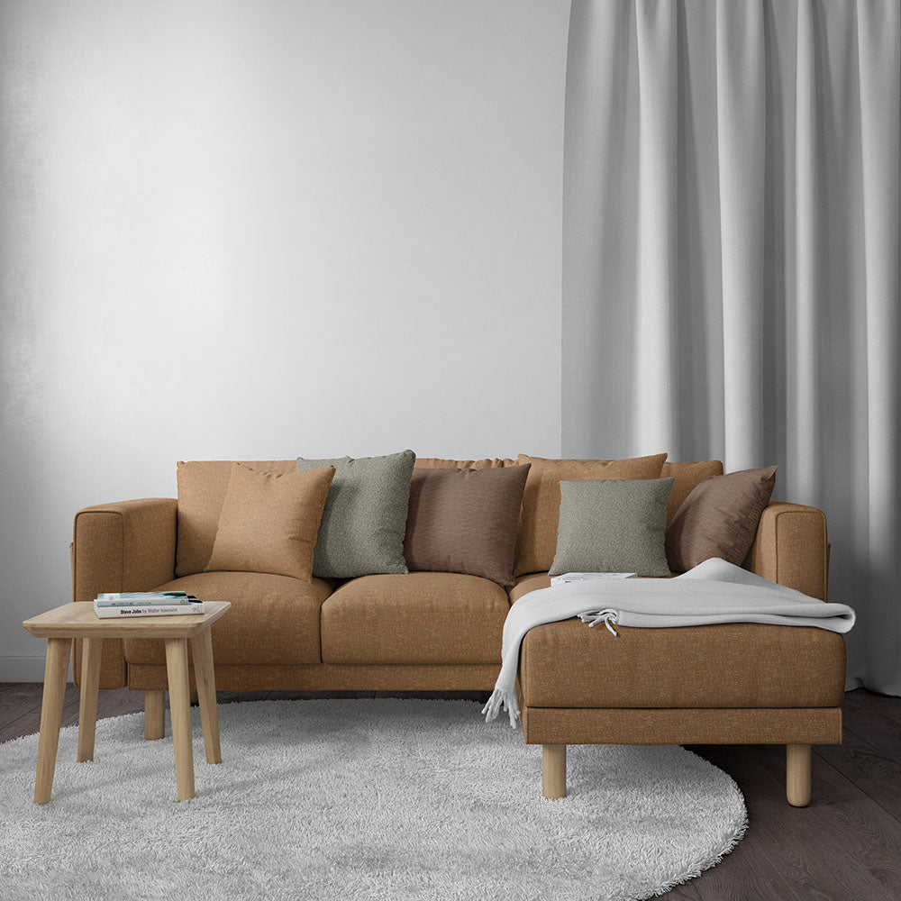 Brown fabric L-shaped sofa with chaise, earth-toned cushions, light wood legs, on a gray rug with a round wooden table.
