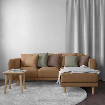 Brown fabric L-shaped sofa with chaise, earth-toned cushions, light wood legs, on a gray rug with a round wooden table.