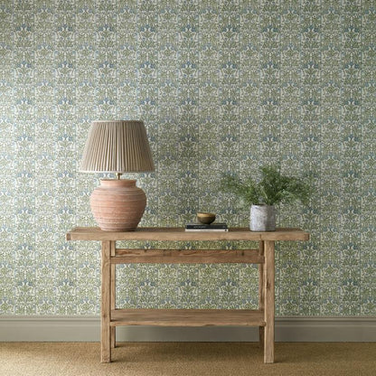 Morris & Co. Oak & Blossom Wallpaper in Thyme and Woad featuring a delicate botanical composition of oak leaves, acorns, and flowering blossoms arranged over a subtle striped background. The elegant green and blue wallpaper design combines stained-glass-inspired details with a textured block-printed effect, creating a sophisticated Arts & Crafts heritage wallcovering for traditional and contemporary interiors, including bedrooms, living rooms, dining rooms, and statement walls.