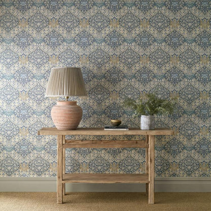 Morris & Co. Norbury Wallpaper in Woad and Linen featuring a refined ogee-shaped damask pattern with flowing floral motifs, leafy details, and an elegant woven-inspired texture. This wide-width heritage wallpaper showcases a sophisticated blue and neutral color palette, blending traditional Arts & Crafts design with timeless William Morris style for luxury bedrooms, living rooms, dining spaces, libraries, and statement walls.