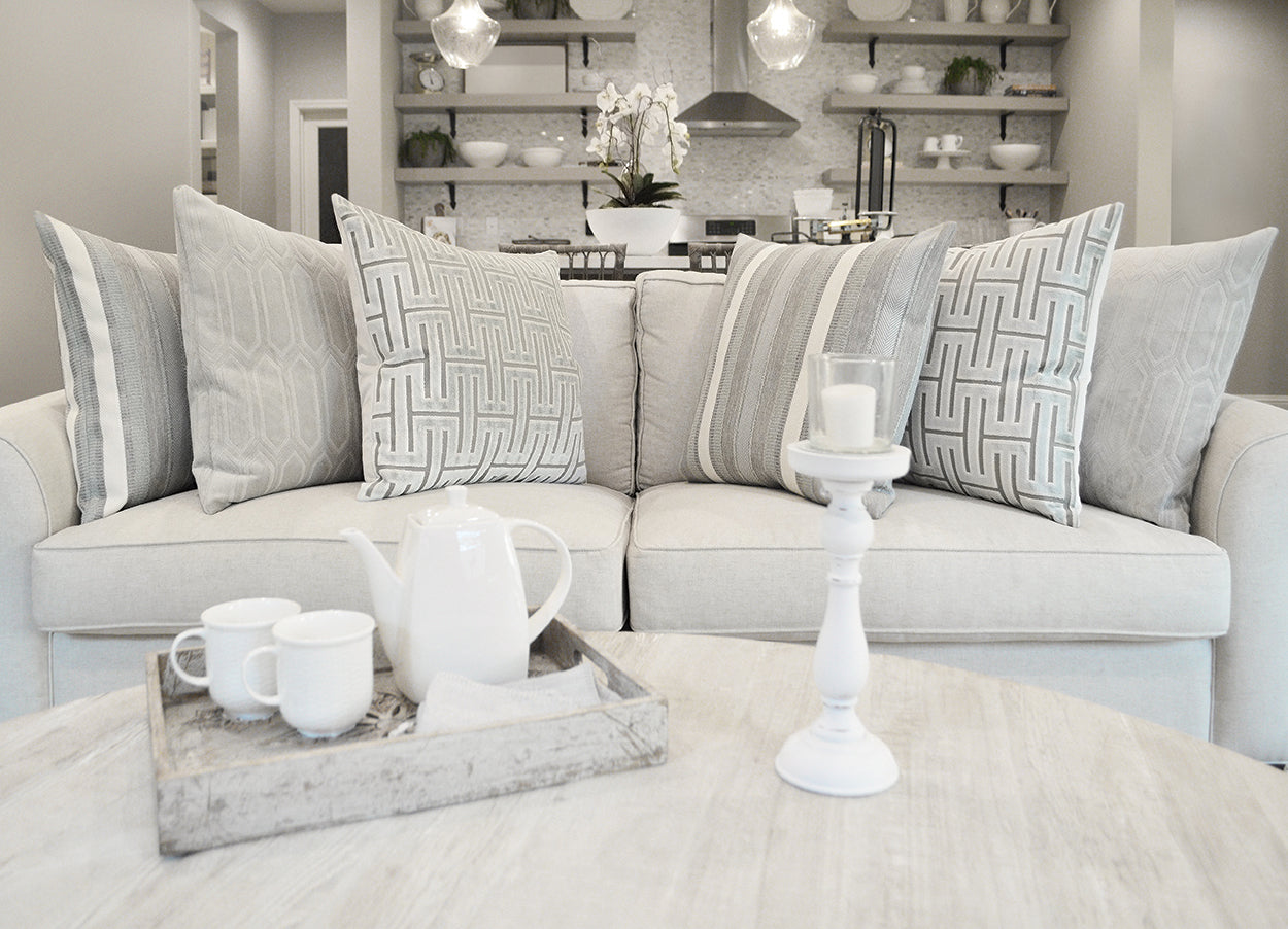 Neutral living room with beige sofa, geometric gray pillows, light wood coffee table, white teapot and mugs on a tray.