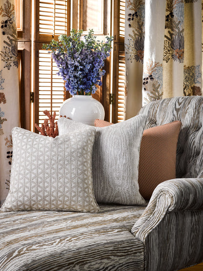 Beige-gray striped sofa with geometric cushions, orange throw pillow, white vase with purple lavender, wood shutters.