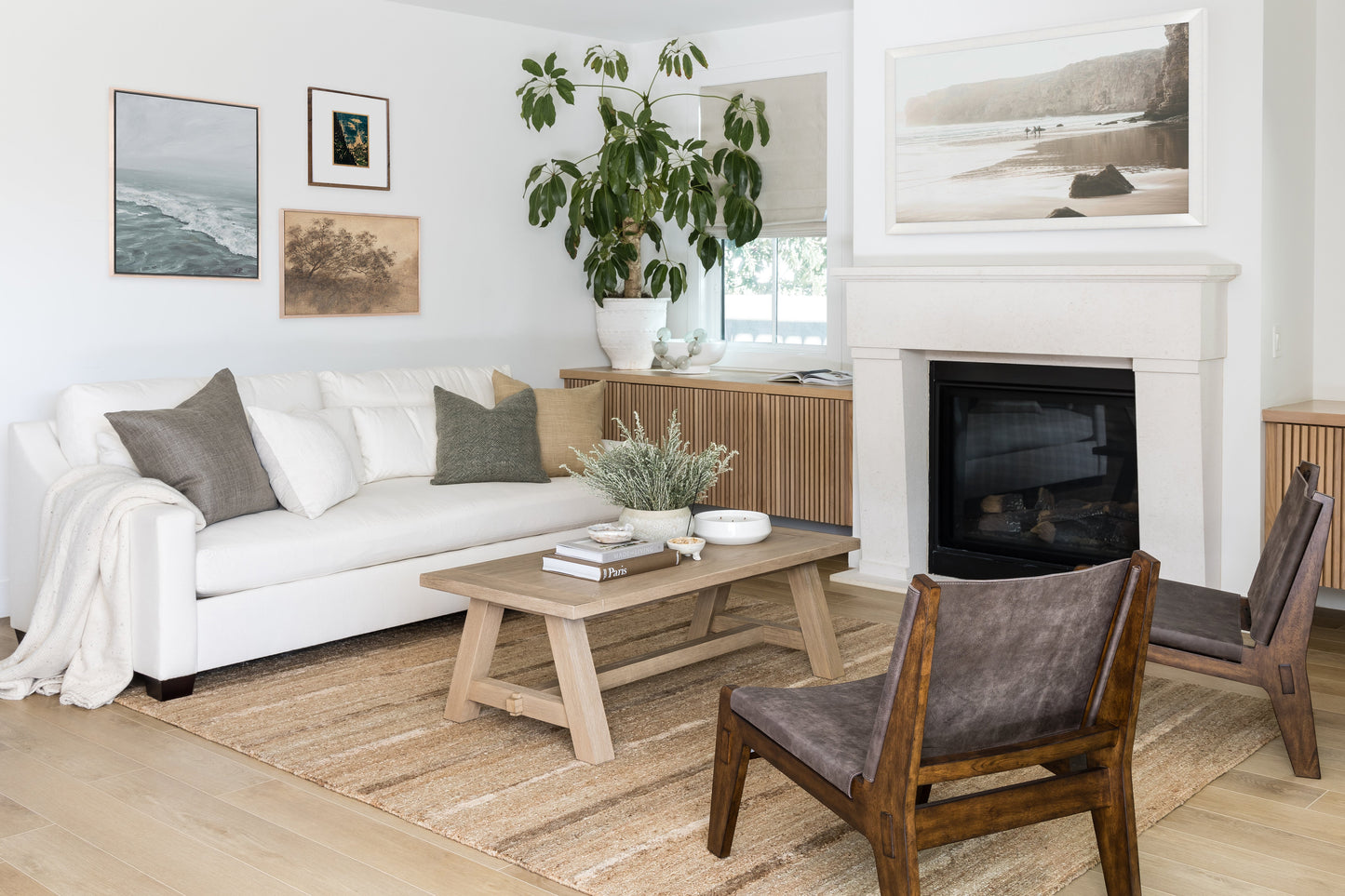 Bright living room with white sofa, neutral cushions, light wood coffee table, mid-century chairs, fireplace, and plant.