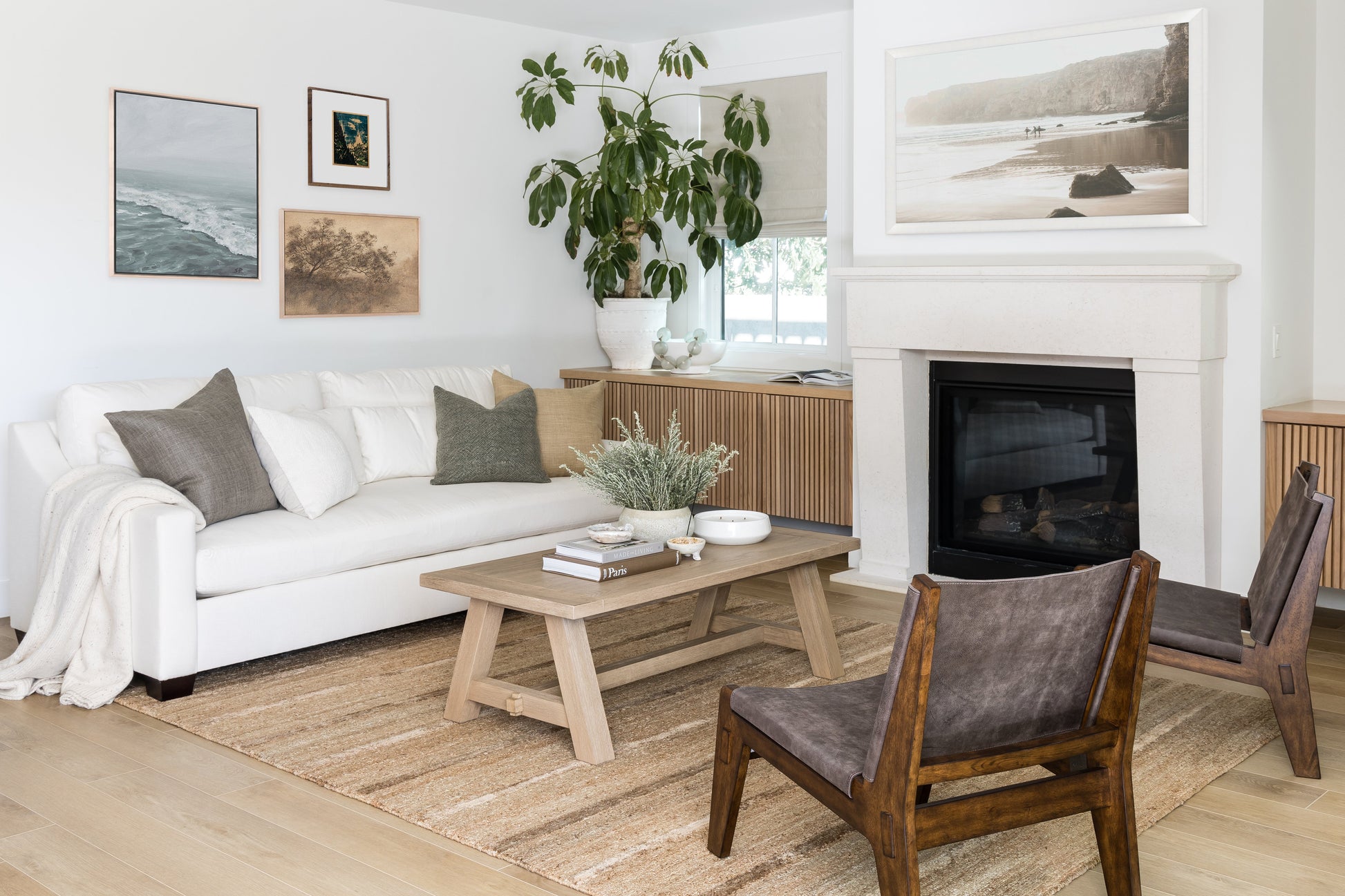 Bright living room with white sofa, neutral cushions, light wood coffee table, mid-century chairs, fireplace, and plant.