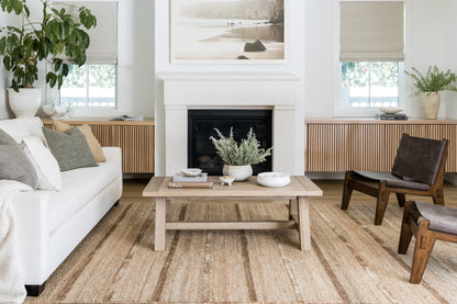 Neutral living room with white sofa, light oak coffee table, beige jute rug, plant, mid-century wooden chairs, fireplace.