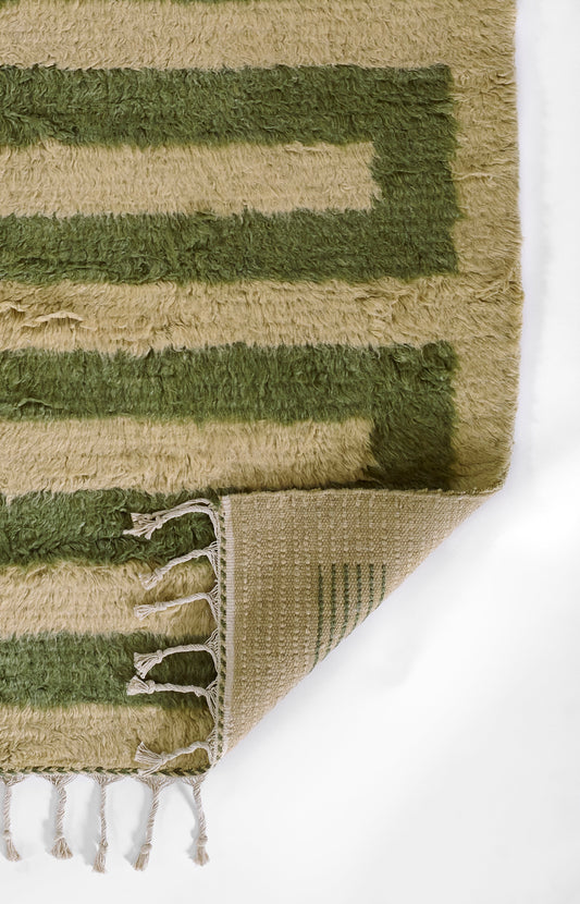 Beige & olive green shag rug with rectangular border stripes; soft pile, fringed edges, folded to reveal the woven back.