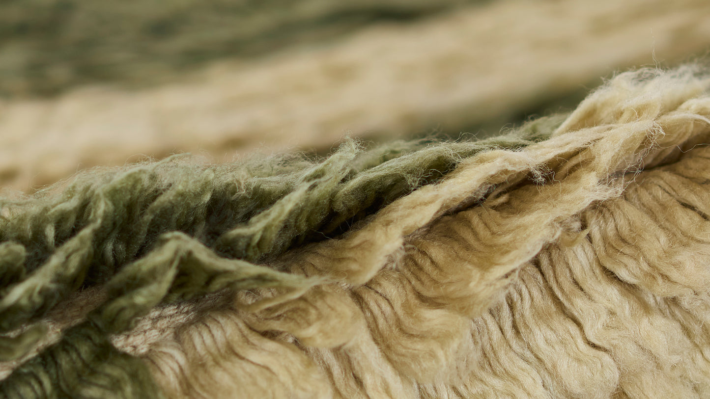 Close-up of olive green and beige chunky wool rug fibers with fluffy, textured pile.