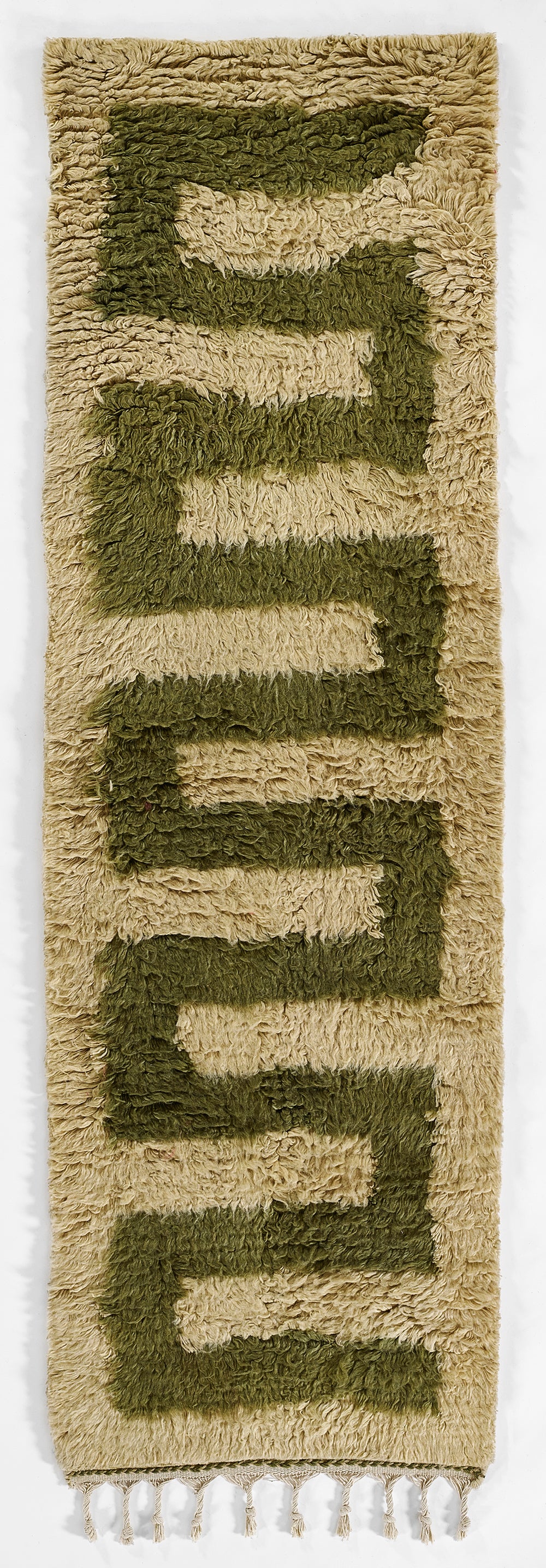 Long beige shag rug with olive-green geometric blocks in a stepped E pattern; plush texture and tassel fringe.