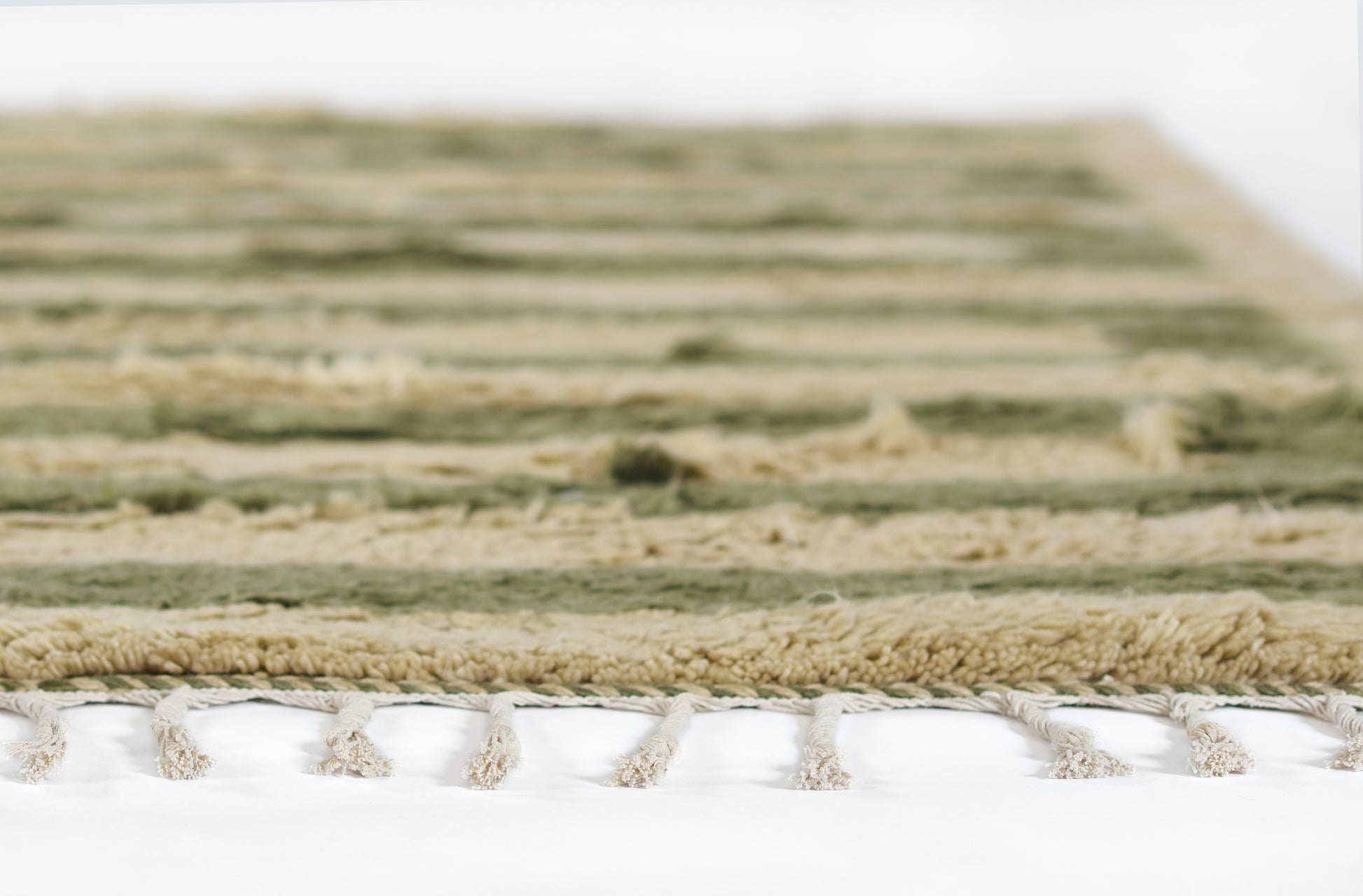 Green and beige striped rug with cream fringe tassels along the edge, soft textured weave.