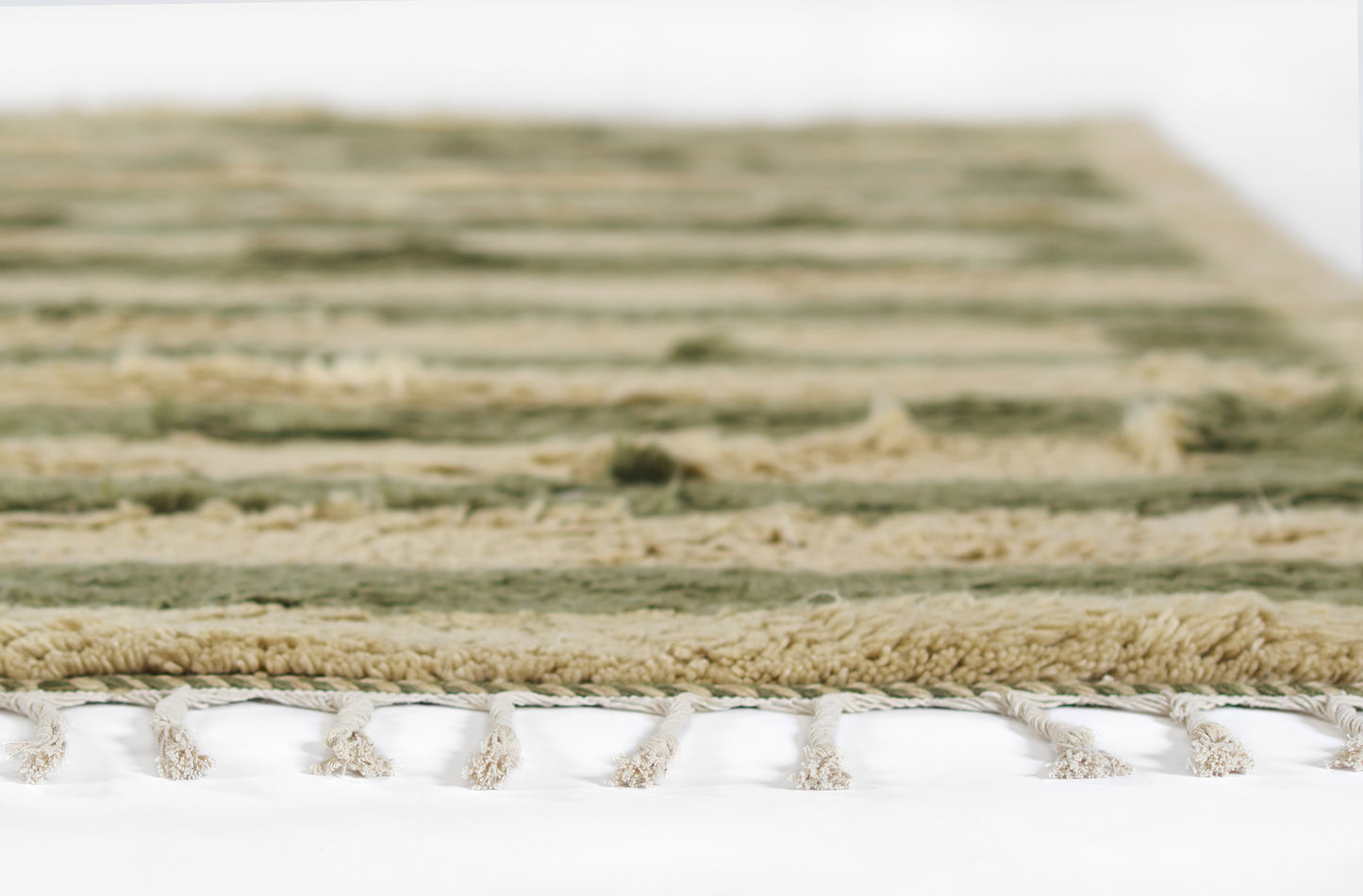 Close-up of a striped green and beige woven rug with off-white fringe tassels along the edge.