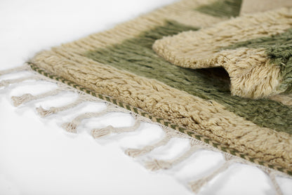 Close-up of an olive green & beige woven rectangular rug with fluffy pile & fringed edge tassels.