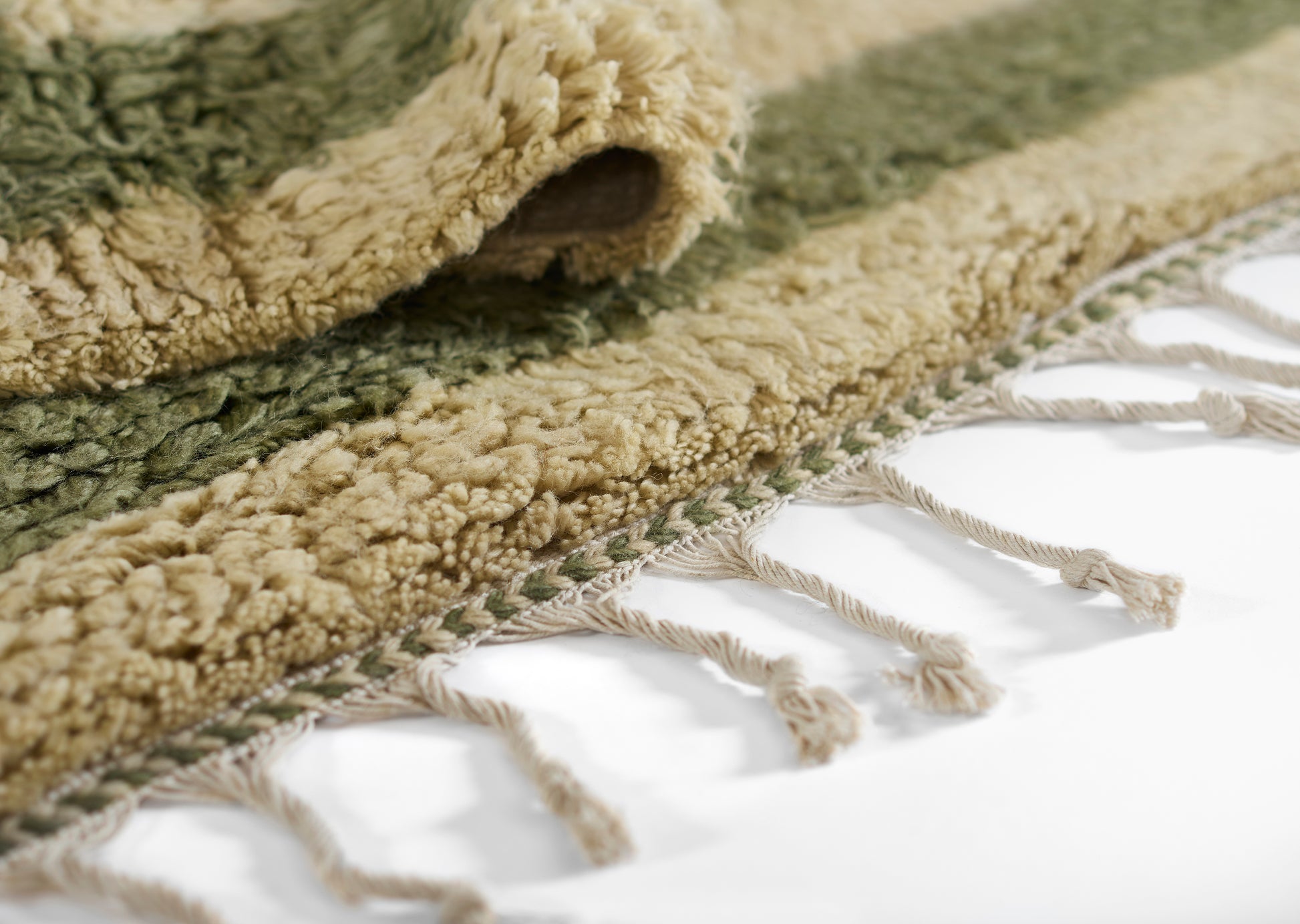 Green and beige textured rug with chunky pile and twisted fringe tassels along the edge