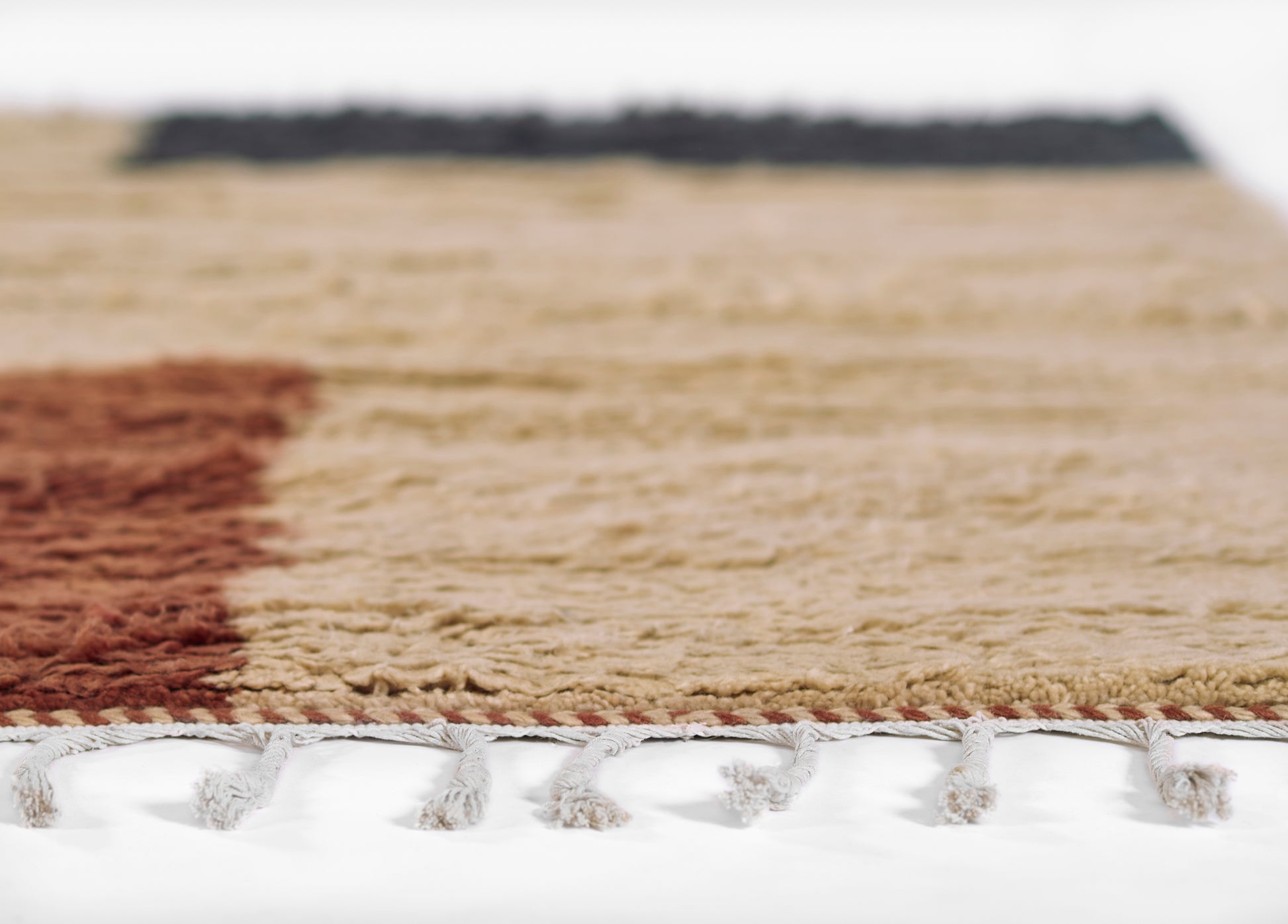 Woven beige rug with a red left border, dark top border, and white tassel fringe along the edge.