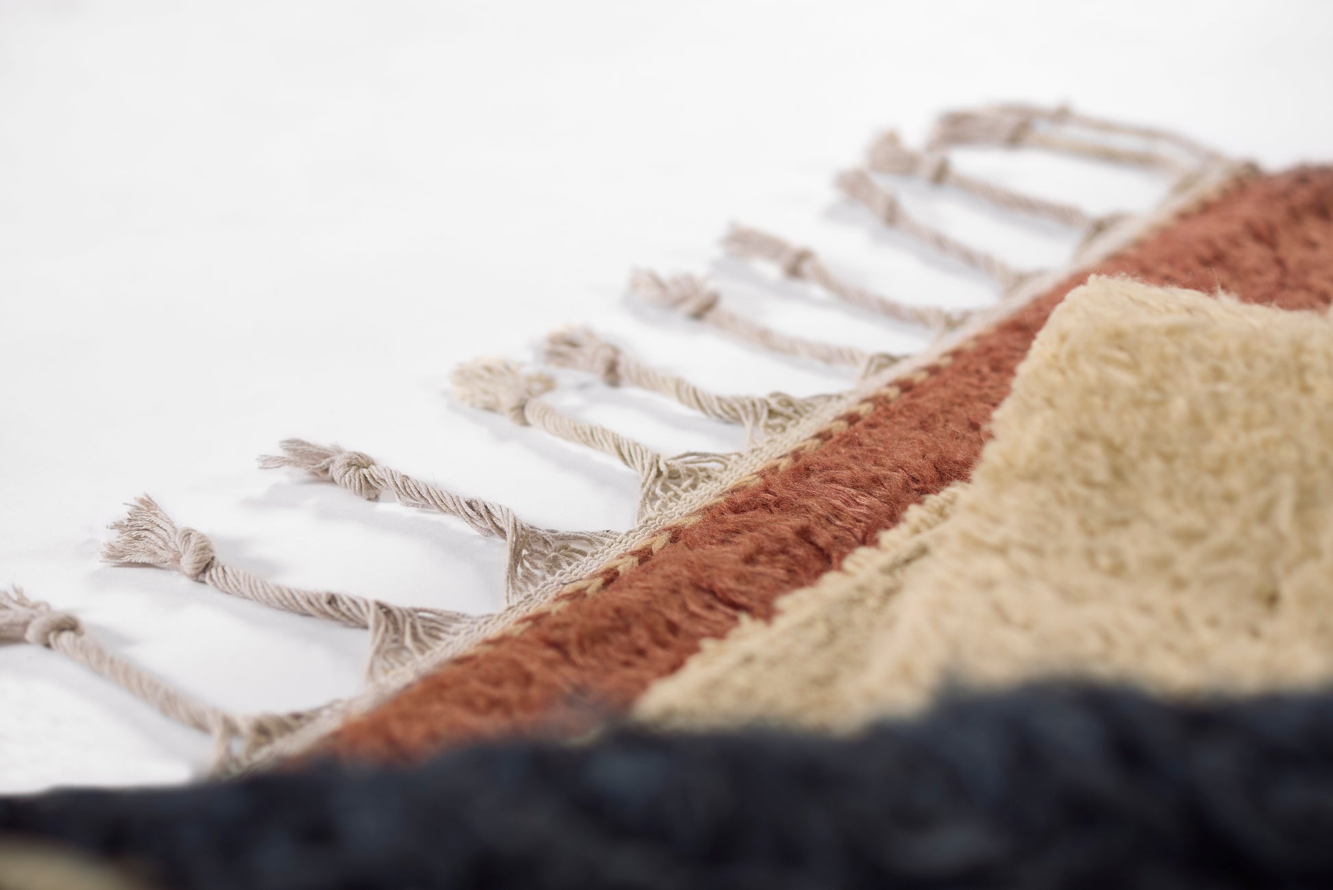 Close-up of woven rug edge with knotted fringe; color blocks in beige, rust orange, cream and navy.