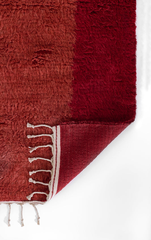 Two-tone burgundy shag rug runner with white fringe tassels along the edge and a folded corner.