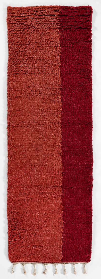 Two-tone long shag rug in orange-red and deep red with fluffy pile and fringe tassels.
