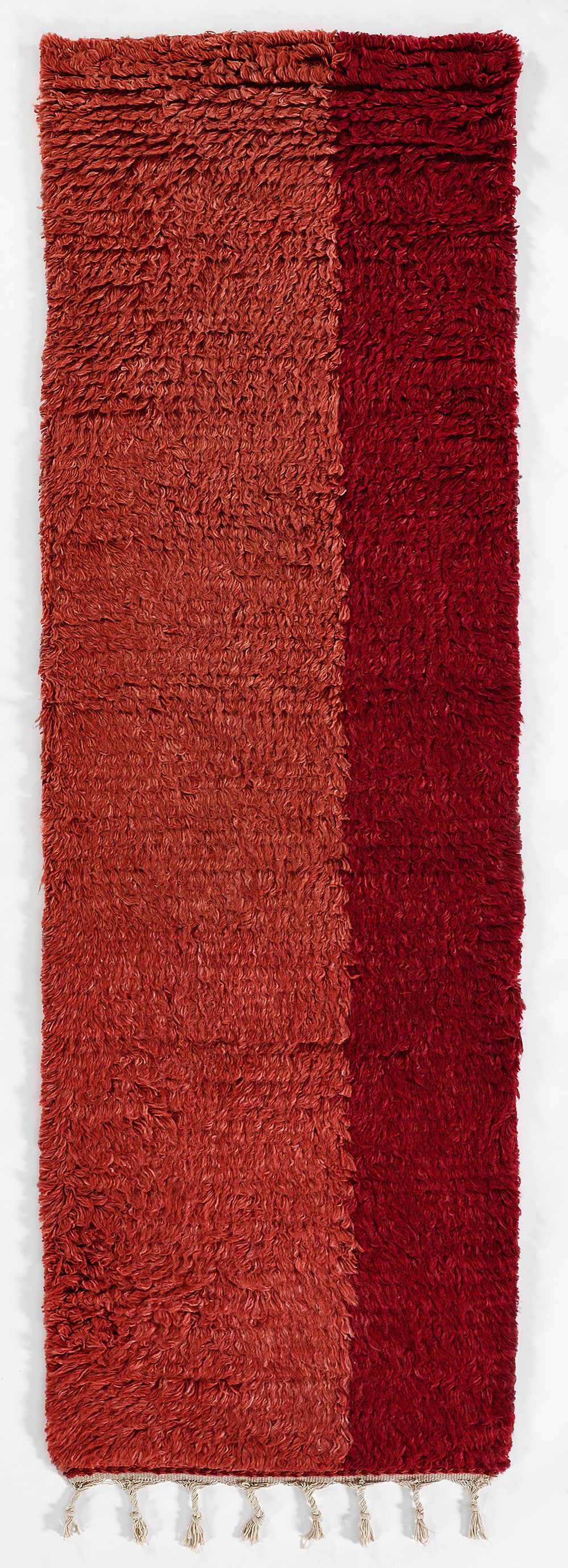 Long shag rug with two-tone red-orange panels and cream fringe along one end.