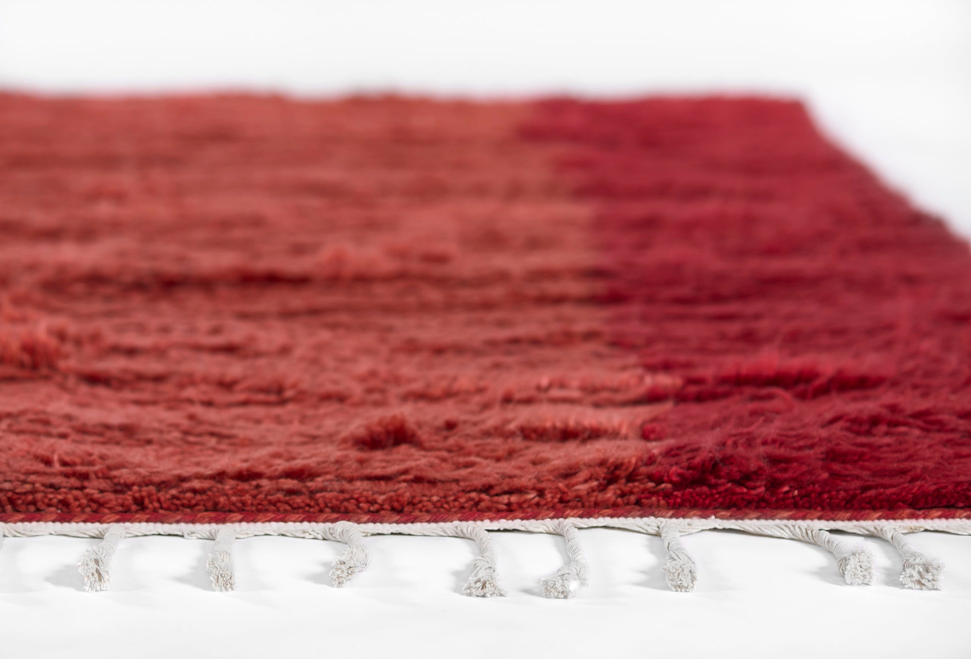 Deep red shag rug with white fringe along edge, plush pile for contemporary home decor.