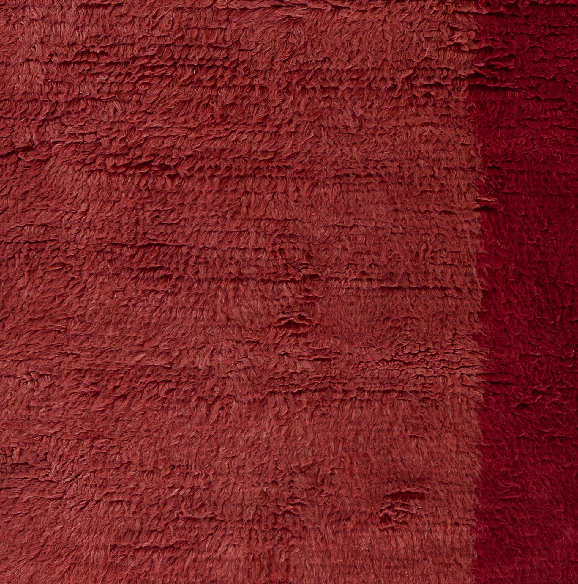 Close-up of fluffy red shag rug fabric with long fibers and a dark crimson edge stripe.