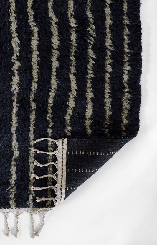 Dark navy shag rug with beige vertical stripes, tassel-fringed edges and dotted border at the corner.